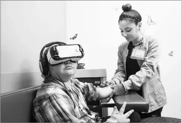  ??  ?? A child uses VR goggles while getting his blood drawn. Such devices allow patients to relax despite the stresses of treatment.