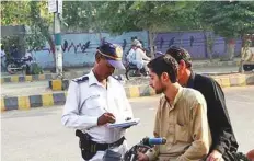  ??  ?? A traffic police officer in Karachi fines a motorcycli­st for not wearing helmet as part of the ongoing traffic campaign.