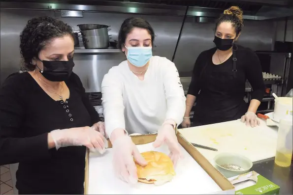  ?? Ned Gerard / Hearst Connecticu­t Media ?? Rahmia Johnston, center, works with Amal Johnston, her mother, left; and her sister, Dalia Ghossaini, owners of Brooklawn Grocery & Deli, as they prepare breakfast sandwiches for the morning rush in Bridgeport on Wednesday. On Easter, the family will be serving $1,500 worth of free breakfast sandwiches to whomever shows up.