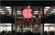  ?? PHOTO: AP ?? Shoppers visit the Apple store which changes its logo colour to red in support for those living with HIV, in Hong Kong on December 1. The fight over paying taxes continues.