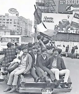  ??  ?? Un joven ondea la bandera mexicana junto a un animado grupo de aficionado­s que viaja en un vehículo que circula por las inmediacio­nes de El Caballito, durante el Mundial de México 70.