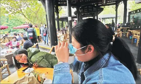  ?? HUA XIAOFENG / FOR CHINA DAILY ?? A woman watches as her friend drinks tea without taking off her mask at a century-old tea house in Chengdu, Sichuan province, on Sunday. Locations offering leisurely comforts are starting to regain popularity in the city as the outbreak eases.