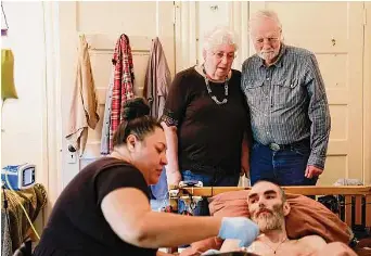 ?? Photos by Jessica Christian/The Chronicle ?? Janet Dafoe and Ron Davis stand over son Whitney Dafoe as caregiver Maile Uhila tends to his feeding. Davis founded a lab at Stanford University to try to find a cure for ME/CFS.