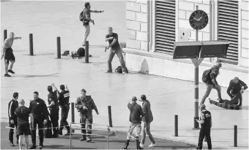  ??  ?? French police (right) turn over and hold the body of a man on the ground while other policemen surround the body of a stabbed woman (rear left), while a soldier (front left) secures the area following an attack at the Saint-Charles main train station...