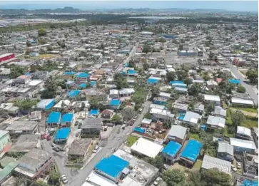  ?? Dennis M. Rivera, AP ?? This June 18, 2018, photo shows an aerial view of the Amelia neighborho­od east of San Juan, Puerto Rico. Thousands of people across Puerto Rico are still living in damaged homes, protected by blue plastic tarps, nine months after Hurricane Maria devastated the island.