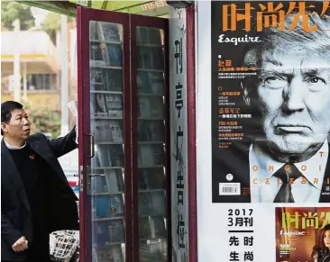  ??  ?? Around the corner: A man standing near a magazine advertisem­ent featuring Trump at a news stand in Shanghai, China.