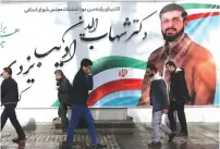  ?? (Nazanin Tabatabaee/WANA via Reuters) ?? PEOPLE WALK past a parliament­ary election campaign poster in Tehran on Saturday.
