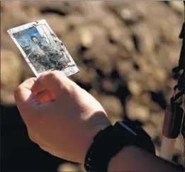  ??  ?? A SEARCHER holds a dirt-covered photograph found along a creek in Montecito. Teams duct-taped their boots on so they wouldn’t lose them in the mud.