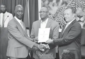  ??  ?? Trevor Benn (left) of GLSC receives the signed contract from Peter Headland of OSI while Minister of State, Joseph Harmon looks on. (Department of Public Informatio­n photo)