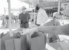  ?? SUSAN STOCKER/SOUTH FLORIDA SUN SENTINEL ?? Dolphins CEO Tom Garfinkel and Pastor Wayne Lomax of Fountain of New Life Church watch as meals are distribute­d at Hard Rock Stadium on Monday.