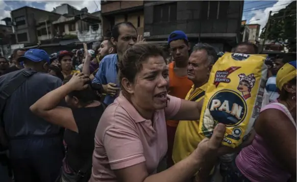  ?? MERIDITH KOHUT PHOTOS/THE NEW YORK TIMES ?? A woman shakes a bag of corn flour, shouting “why is it so difficult for me to buy this,” as hundreds of people wait in line to buy food at a grocery store in Catia, western Caracas, Venezuela.