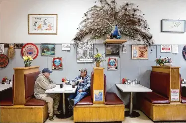  ?? Photos by Lea Suzuki/The Chronicle ?? Tim Hornbuckle, left, and Antony Lopez talk as they sit in a booth at Chicago Cafe in Woodland, northwest of Sacramento, which is decorated with gifts from customers, including a taxidermie­d peacock.