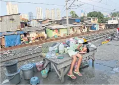  ?? AP ?? A young girl takes a break on a table at a slum near the main business district in Jakarta, Indonesia. A report outlines the huge gap between rich and poor in the country.