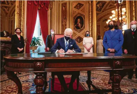  ?? Jim Lo Scalzo / Pool / AFP via Getty Images ?? President Joe Biden signs documents in his first hours in the Oval Office as Vice President Kamala Harris observes. Biden issued executive orders to reverse policies on climate change and immigratio­n put in place by former President Donald Trump.