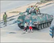  ?? AFP ?? Young women walk past an armoured vehicle stationed by an intersecti­on as Zimbabwe soldiers regulate traffic in Harare.