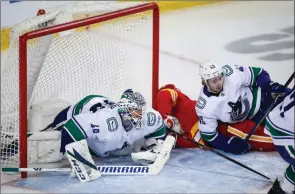  ??  ?? The Canadian Press
Vancouver Canucks goalie Braden Holtby and Quinn Hughes crash into the net with Calgary Flames’ Elias Lindholm during third-period NHL action in Calgary, Wednesday.