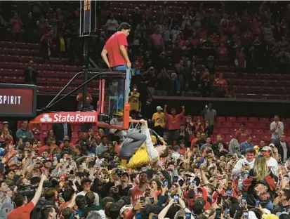  ?? KEVIN RICHARDSON/BALTIMORE SUN ?? Maryland men’s basketball fans storm the court and hang from the basket after the team beat No. 3 Purdue on Thursday night at Xfinity Center in College Park.