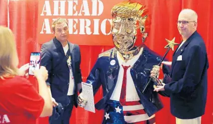  ?? STEPHEN M. DOWELL/ORLANDO SENTINEL ?? Attendees are photograph­ed with the wildly popular “Golden Don” statue of former President Donald Trump in the exhibit hall at CPAC at the Hyatt Regency in Orlando on Friday.