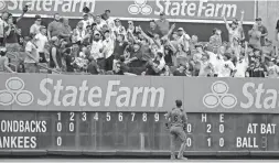  ??  ?? Diamondbac­ks left fielder David Peralta watches as fans fight for a home run ball hit by the Yankees' Mike Tauchman on Wednesday in New York.