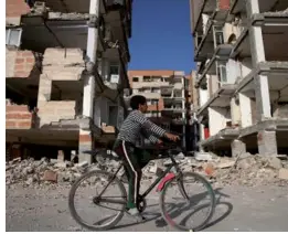  ?? VAHID SALEMI / AP ?? An earthquake survivor rides his bicycle in front of damaged buildings in Sarpol-e-Zahab in western Iran on Wednesday. Survivors are awaiting badly needed aid three days after a powerful earthquake along the Iraq border killed hundreds and left...