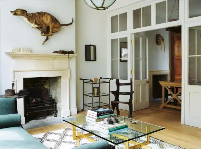  ??  ?? A Grecian revival, ebony Hanbury sofa sits in the window of Fisher’s first-floor sitting room. The French coffee table, in brass with a glass top, stands on a Moroccan Beni Ourain rug. A stuffed greyhound races above the 19th-century Painswick stone,...