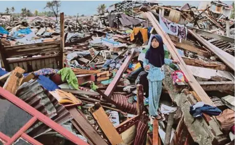  ??  ?? Seorang kanak-kanak berdiri di atas lokasi bekas rumah keluargany­a yang musnah di Palu.