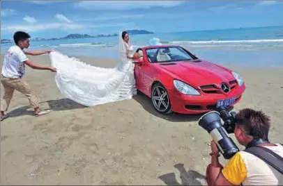  ?? LUO YUNFEI / CHINA NEWS SERVICE ?? A woman poses for wedding photos beside a convertibl­e on a beach in Sanya, Hainan province.