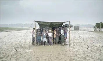  ?? — AFP ?? Rohingya refugees take shelter from the rain during a food distributi­on at Nayapara refugee camp in Bangladesh’s Ukhia district.