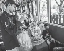  ?? JUNI KRISWANTO / AGENCE FRANCE-PRESSE ?? A bus conductor collects used plastic bottles as fare payment on board a bus in the Indonesian city of Surabaya on July 21.