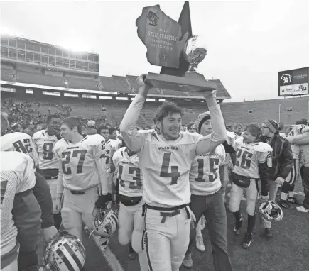  ?? MARK HOFFMAN / MILWAUKEE JOURNAL SENTINEL ?? Rice Lake quarterbac­k Sam Bliese hoists the championsh­ip trophy Friday after the Warriors’ 25-3 victory over New Berlin Eisenhower in the WIAA Division 3 state football title game.