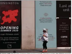  ?? (AP/Alastair Grant) ?? A woman walks Wednesday past two retail spaces currently closed in London. The British economy shrank by 20.4% in the second quarter of this year.