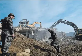  ?? POOL GETTY IMAGES ?? A South Korean soldier stands guard as constructi­on equipment destroys a guard post in the Demilitari­zed Zone. The two Koreas began destroying guard posts under a plan to reduce tensions on the border.