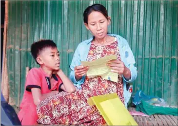  ?? HENG CHIVOAN ?? Klien Savoeun, at seven months pregnant, reads over her one-month contract while her young son looks on in Kandal’s Sa’ang district.