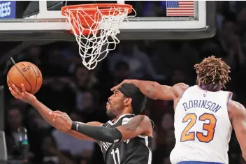  ?? — AP ?? New York Knicks center Mitchell Robinson (right) defends against Brooklyn Nets guard Kyrie Irving who goes up for two points during the first half of an NBA game on Friday.