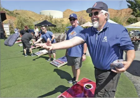  ?? Dan Watson/The Signal ?? Board member Brian Koehn, center, looks on as Scott Shepard, director of Avenues Supported Living Services, warms up for the 6th Annual Cornhole Tournament at Lucky Luke Brewery in Valencia to benefit Avenues Supported Living Services on Saturday.