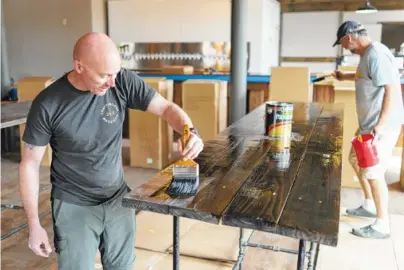  ?? STAFF PHOTOS BY DAN HENRY ?? Chris Calhoun, left, owner/operator of the Tap House in St. Elmo, works on finishing tables in the new bar which he hopes to have ready to open on the first of April.