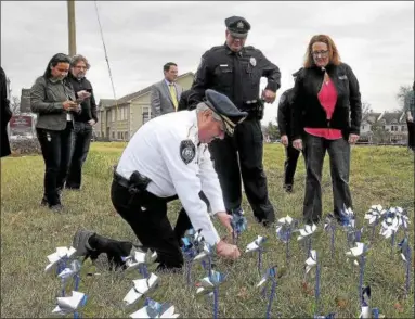  ?? GENE WALSH — DIGITAL FIRST MEDIA ?? Lansdale police Chief Robert McDyre kneels down to plant a pinwheel into the ground Thursday during Mission Kids Advocacy Center’s annual Pinwheel Garden planting to honor child abuse victims.