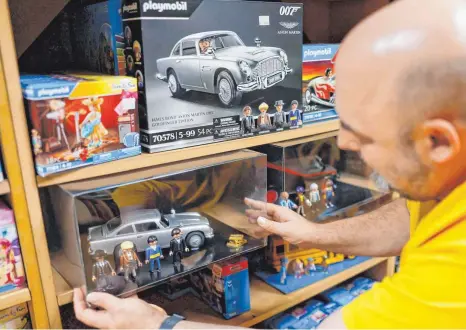  ?? FOTO: DANIEL LÖB/DPA ?? Stefan Will stellt ein Playmobil-Auto, den Aston Martin DB5 aus der James Bond/007 „Goldfinger“-Edition mit vier Spielfigur­en, in ein Regal. Diese Playmobil-Spielwelt mit lizenziert­en Figuren oder Autos aus berühmten Serien und Filmen richtet sich an erwachsene Sammler.