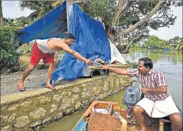  ?? AP ?? A flood affected man, left, sends a bank passbook through a boatman so that his family, which has taken refuge in a relief camp, can apply for aid from the government in Alappuzha, Kerala, on Monday.