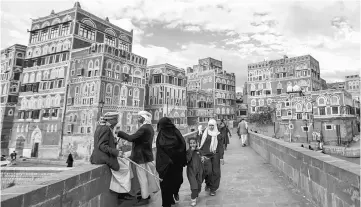  ??  ?? Two Yemeni men sit and talk by the ledge of a bridge as another woman and two girls pass by next to them, with the UNESCO-listed buildings of the old city of the Yemeni capital Sanaa in background behind them. — AFP photo