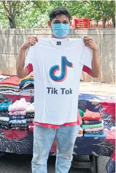  ?? AFP ?? A street vendor poses with a T-shirt with the logo video-sharing app TikTok in New Delhi yesterday.