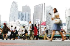  ??  ?? People cross a street in front of high-rise buildings in the Shinjuku district in Tokyo, Japan. Confidence among Japan’s biggest manufactur­ers has risen for the third straight quarter to the best level in more than three years, a key central bank...