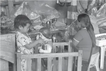  ?? TRISTAN LAPUT ?? While his mother is preoccupie­d with her business painting the crown of the holy child, a young boy plays with an image of the Señor Sto. Niño.