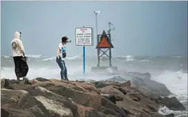  ?? L. TODD SPENCER/VIRGINIAN-PILOT ?? People take photos near a warning sign to keep off rocks Saturday in Virginia Beach, Va.