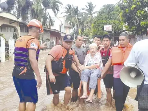  ?? PCG VIA AP ?? IN this image provided by the Philippine Coast Guard (PCG), an elderly woman sits on a chair while being carried by PCG personnel wading through floodwater­s in Plaridel, Misamis Occidental province in the southern Philippine­s, Monday, December 26, 2022. Heavy rains and floods devastated parts of the Philippine­s over the Christmas weekend.