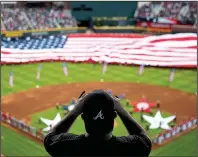  ?? AP/DAVID GOLDMAN ?? A spectator takes a photo of a United States flag during the national anthem at a recent Major League Baseball game between Atlanta and Washington. The anthem has been a part of U.S. sports games since World War II, with some experts agreeing that Game...