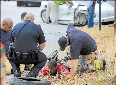  ?? Arkansas Democrat-Gazette/STATON BREIDENTHA­L ?? Little Rock police officers and firefighte­rs help an injured man, who was a suspect in a disturbanc­e, after the man reportedly jumped in the passing car of Little Rock City Director Doris Wright on Tuesday afternoon, causing her to crash the vehicle.