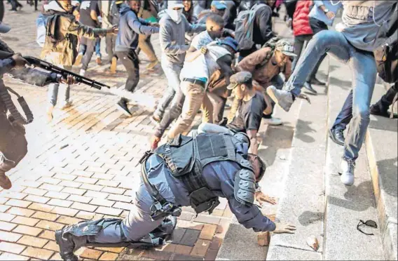  ?? Photo: Marco Longari/AFP ?? Scenes of chaos: During a clash between students and police at the University of the Witwatersr­and on Tuesday an officer falls and a colleague fires rubber bullets at fleeing students.