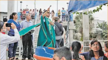  ??  ?? El sacerdote, antes del desfile náutico, les da la bendición a las embarcacio­nes.