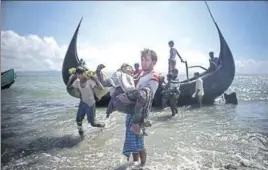  ?? AFP ?? A Bangladesh­i man helps Rohingya refugees disembark from a boat on the Naf river shoreline after crossing the border from Myanmar in Teknaf on September 30.